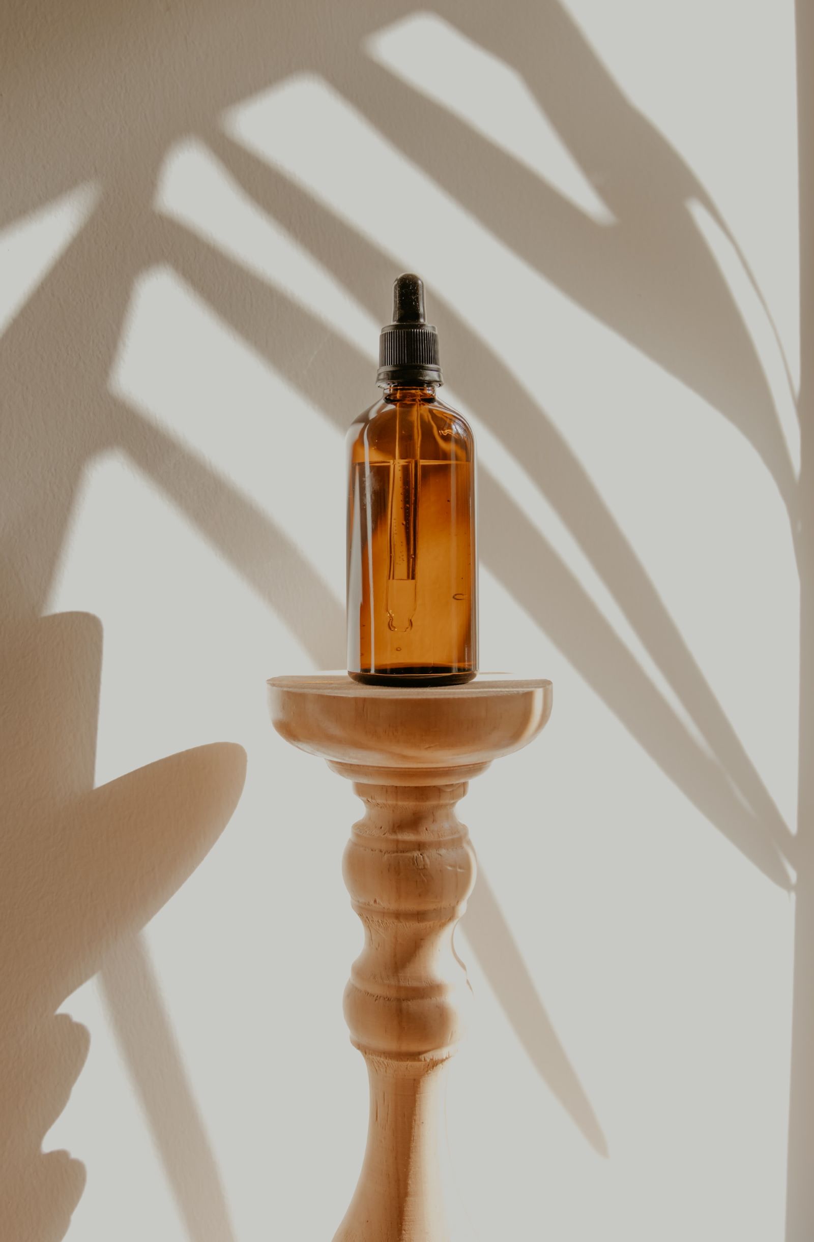 Brown glass bottle of essential oil on wooden stand and the shadow of a plant behind it