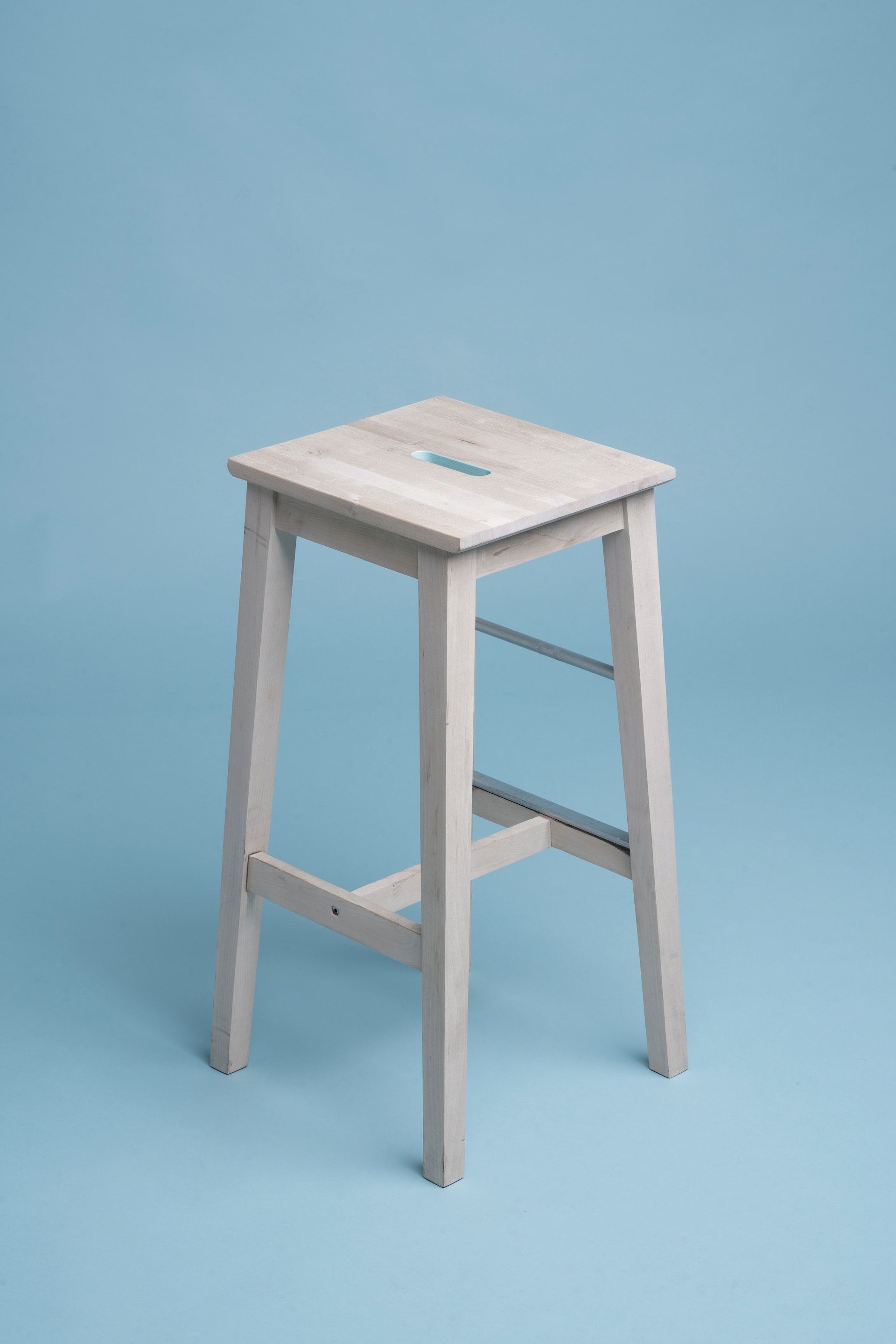 A gray, wooden stool with blue studio wallpaper beneath and behind it